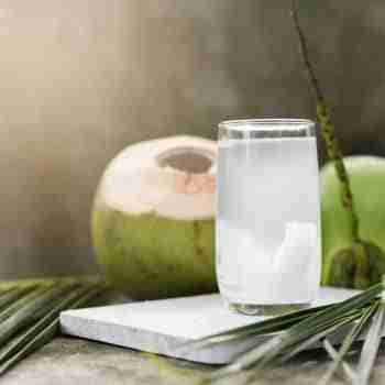 a glass of fresh coconut water on a table surrounded by coconuts