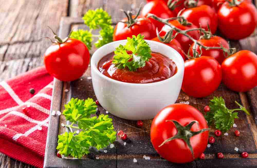 a freshly made cup of tomato sauce on a wooden cutting board surrounded by tomatoes on a sunny day