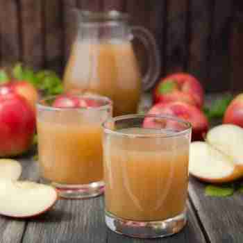 a jug and two glasses of fresh cloudy apple juice with red apples