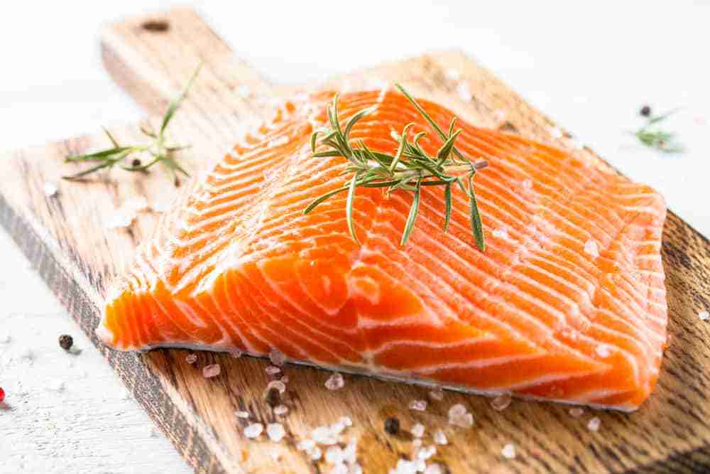 an uncooked salmon fillet on a wooden chopping board with a sprig of time and sea salt