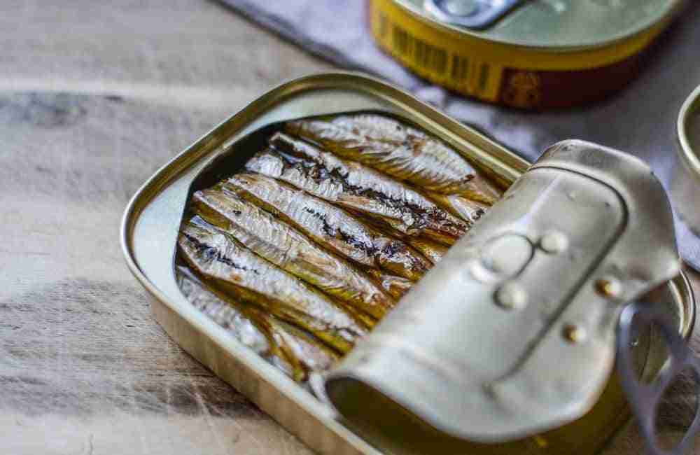close up of an opened tin of sardines on a wooden kitchen table
