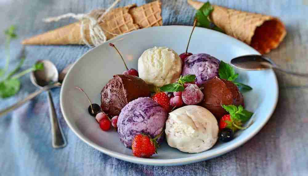 a bowl of five scoops of different flavor ice cream accompanied by summer berries