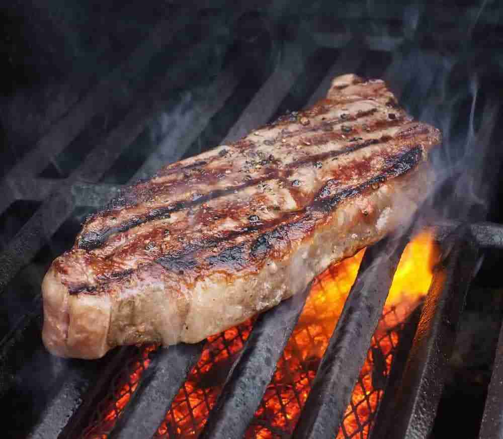 close up of a sizzling beef steak on a flaming grill