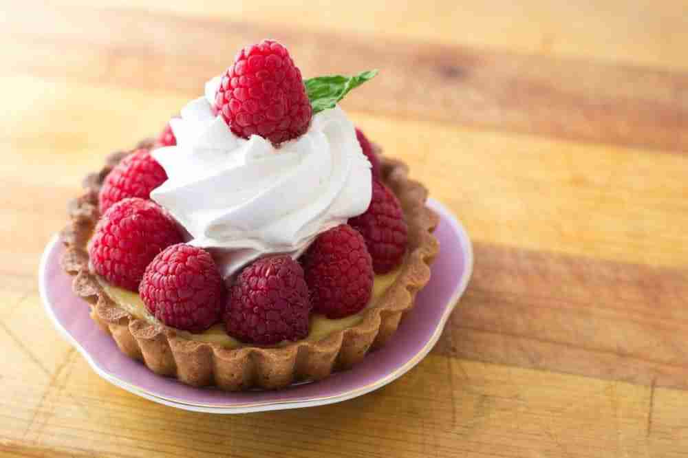a strawberry and whipped cream tart presented on a plate on a wooden table top