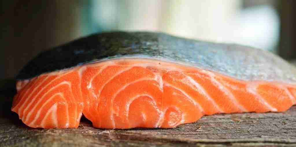 an uncooked salmon fillet with skin to one side on a wooden chopping block